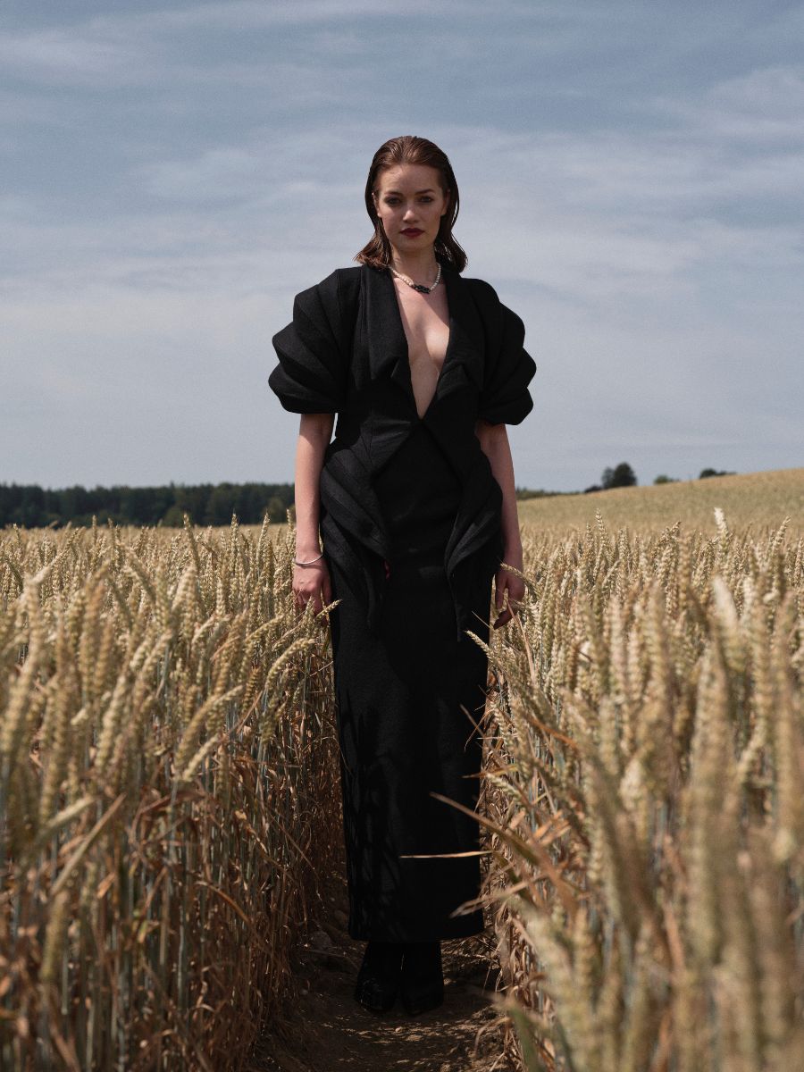 Frau im schwarzen Kleid mit Puffärmeln steht im Kornfeld – Editorial Styling von Julia Ebert.