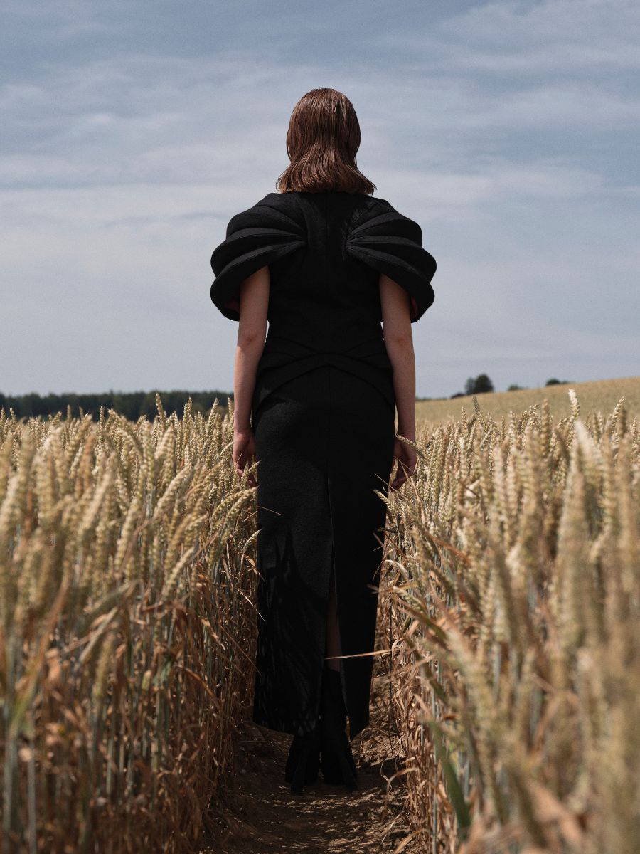 Rückansicht einer Frau im schwarzen Kleid im Kornfeld – Editorial Hair & Make-up