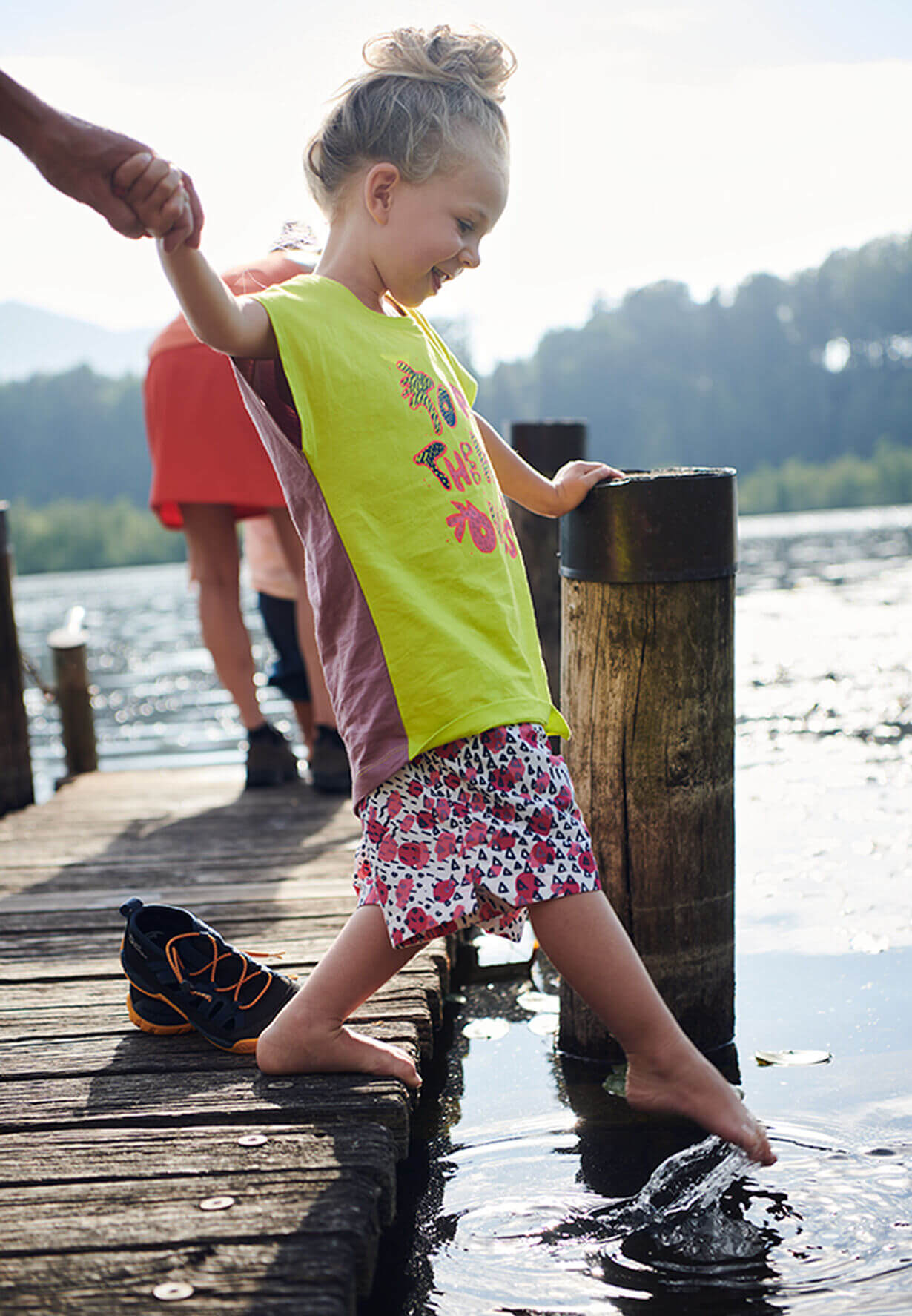 Fotoshooting - kleines Mädchen steht auf einem Steg am See und hält einen Fuß ins Wasser, Styling von Julia Ebert.